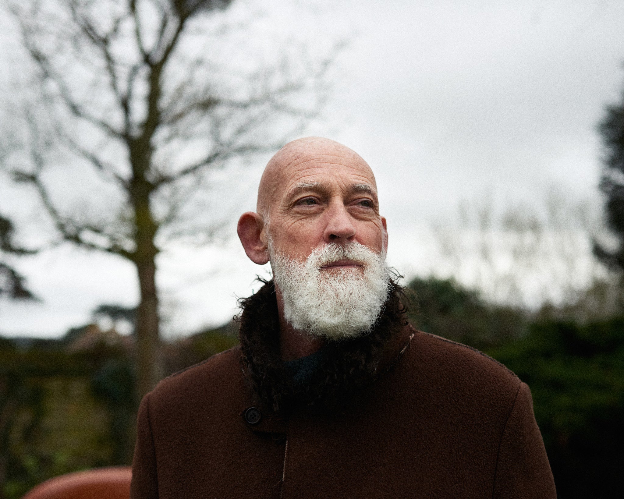 Ross Lovegrove, designer, standing outdoors. Lovegrove has a snow-white beard and is bald, he is interviewed by A Collected Man London