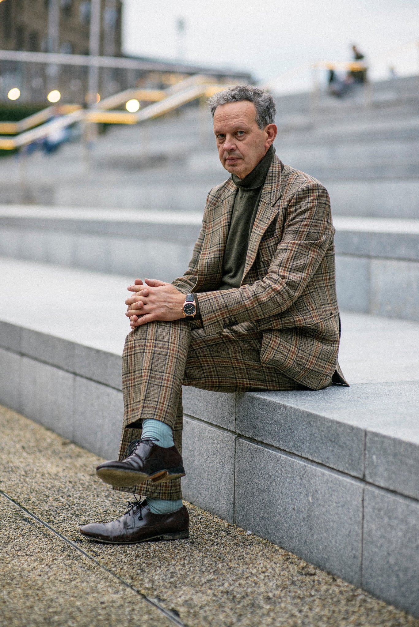 Dixon in a brown suit, sitting on some gray steps